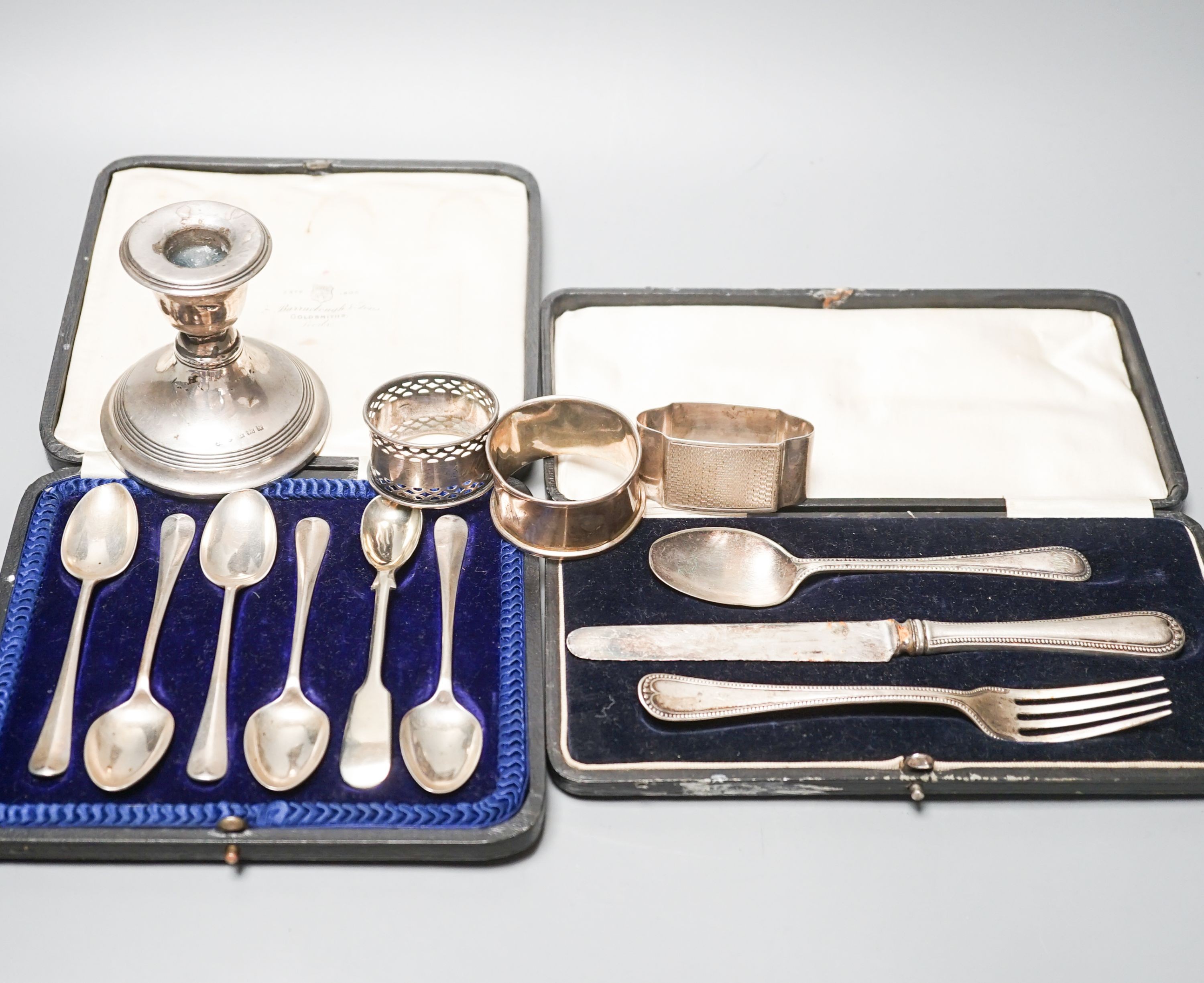 A cased set of six silver teaspoons, a cased christening set, three silver napkin rings and a silver dwarf candlestick.